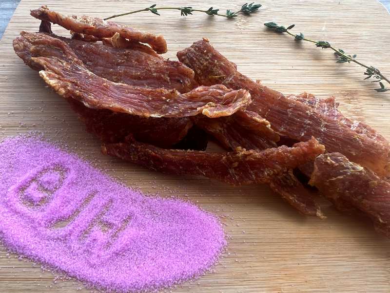 Jerky beside a bright pink mound of salt on a board