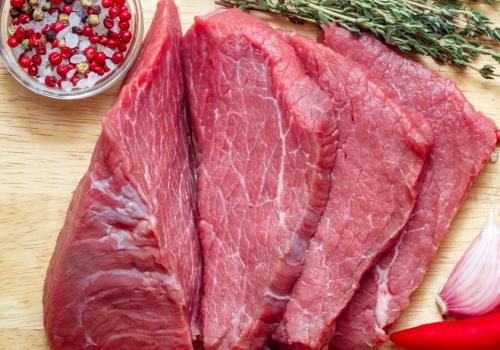Thin raw beef slices beside herbs and peppercorns