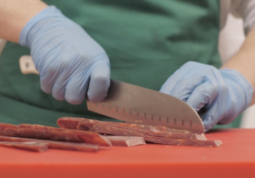 Gloved hands slicing raw meat on a red cutting board