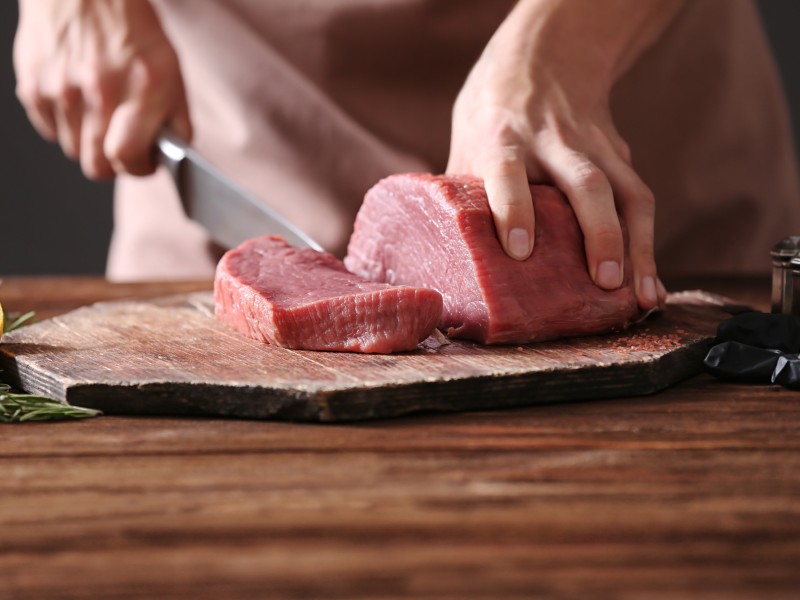 Hands slicing a piece of raw meat on a cutting board