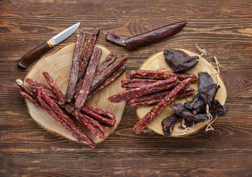 Assorted dried meat strips on a board beside a knife