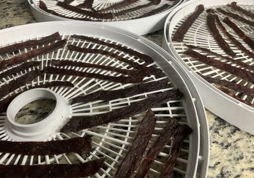 Dried beef strips across several white dehydrator trays
