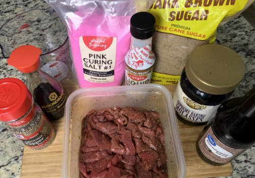 Thin beef strips coated in marinade with the ingredients behind them