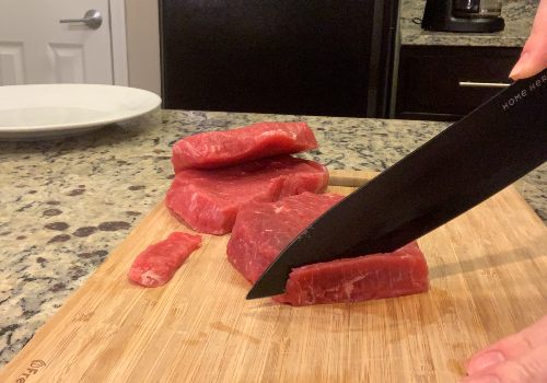 A cook slicing firm beef on a wooden board