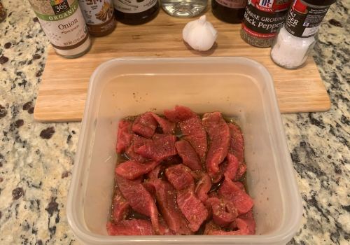 Beef strips in marinade with garlic and sauces behind them
