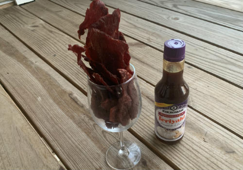 Teriyaki jerky in a stemmed glass beside a Kikkoman bottle