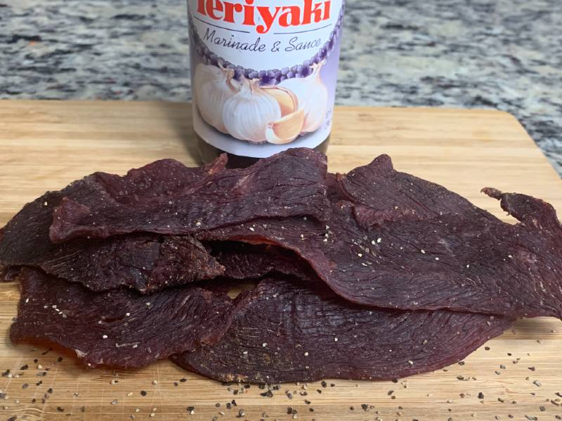 Homemade teriyaki jerky piled below a Kikkoman marinade bottle