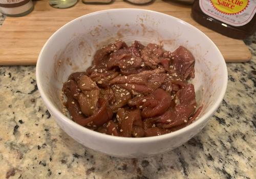 Beef strips coated with sesame-studded marinade in a bowl