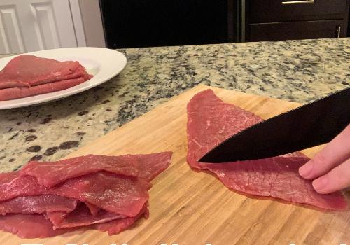 Thin beef slices being cut into narrower strips
