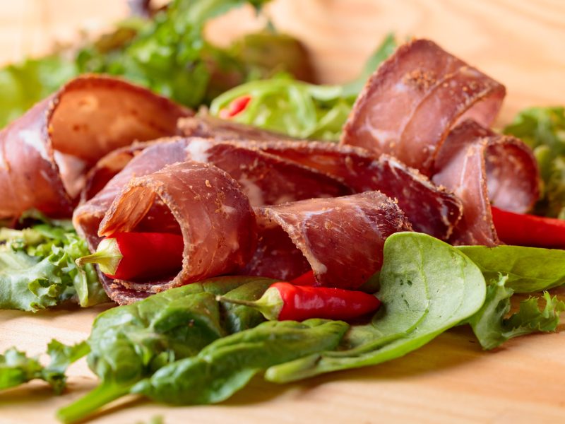 Thin slices of cured meat arranged over salad greens