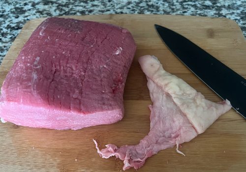 A roast beside a removed strip of fat and a knife