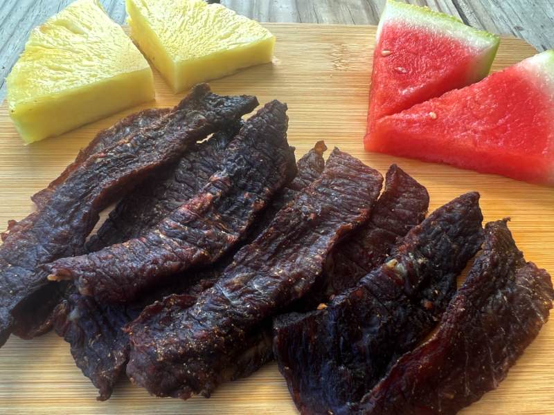 Homemade jerky strips beside pineapple and watermelon wedges