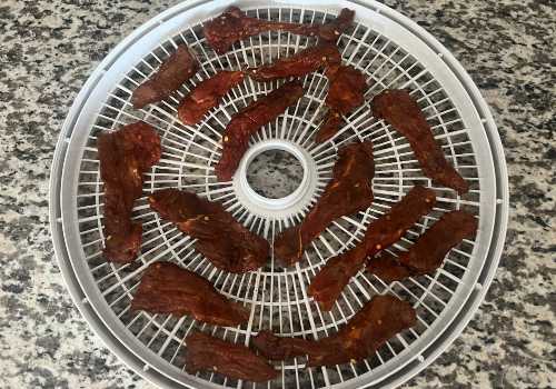 Marinated chile-coated beef strips arranged on a dehydrator tray