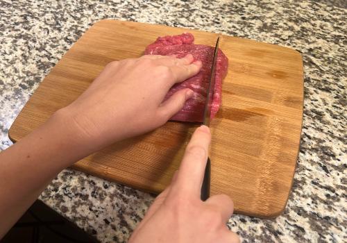 A cook slicing raw beef into long strips