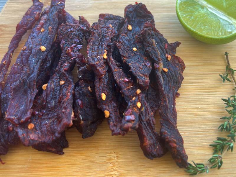 Dark chile-coated jerky strips with lime and thyme on a board