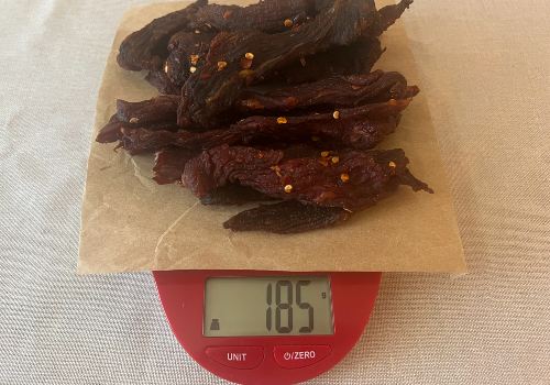 Finished chile-seasoned jerky on a scale reading 185 grams