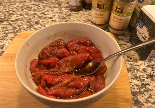 Beef strips being stirred in a bowl of seasoned marinade