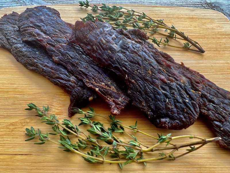 Dark homemade jerky strips arranged beside thyme