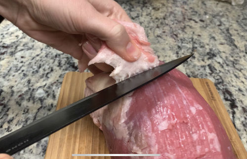 A knife separating a layer of fat from an eye of round roast