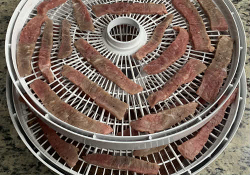 Narrow beef strips spread around a dehydrator tray