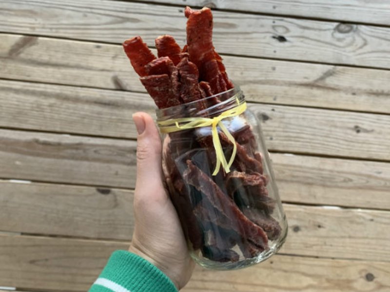 A hand holding a glass jar filled with long jerky strips