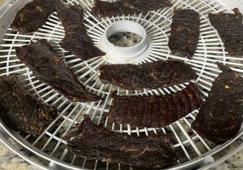 Dark peppered jerky pieces on a dehydrator tray