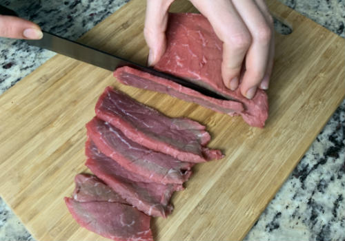 A cook cutting beef into long, thin strips