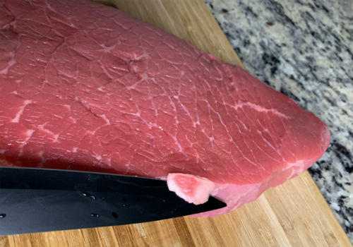 A knife removing a small piece of fat from the beef