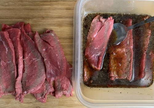 A beef strip being lowered into a container of pepper marinade
