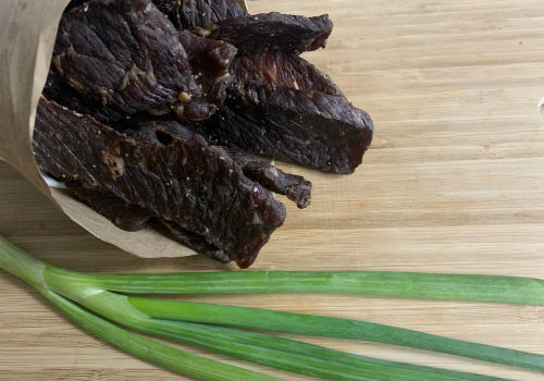 Peppered jerky spilling from a paper bag beside scallions