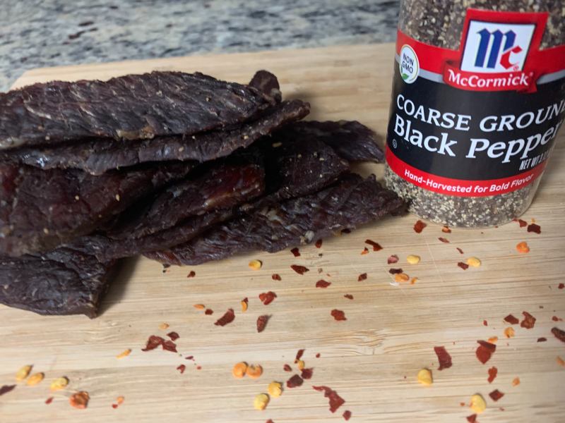 Peppered beef jerky beside a jar of coarse black pepper