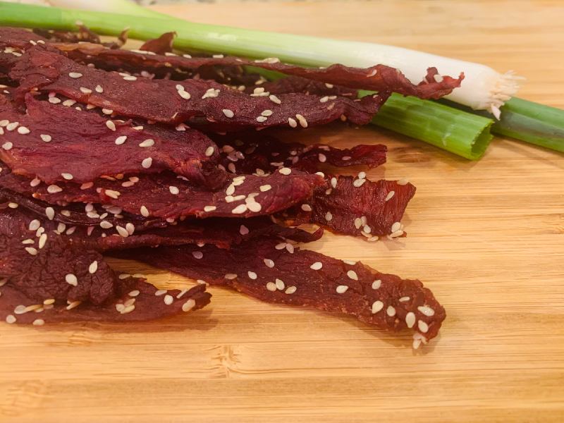 Sesame-speckled jerky strips beside scallions
