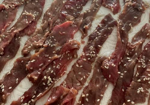 Sesame-coated marinated beef strips draining on paper towels