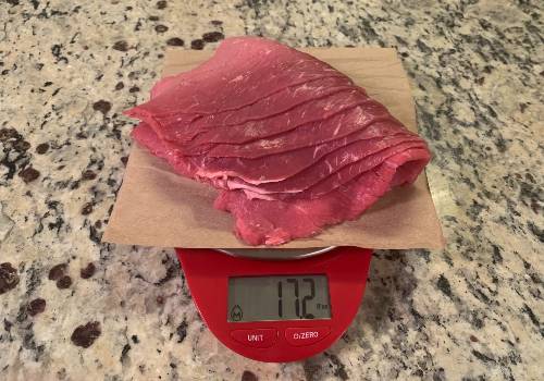 Raw thin-cut beef weighed in ounces on a kitchen scale