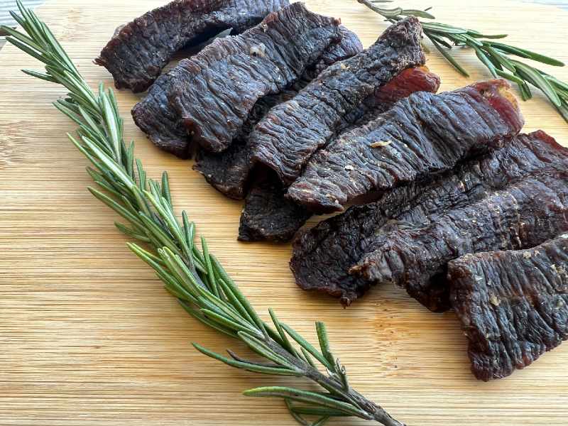 Dark jerky strips arranged beside rosemary