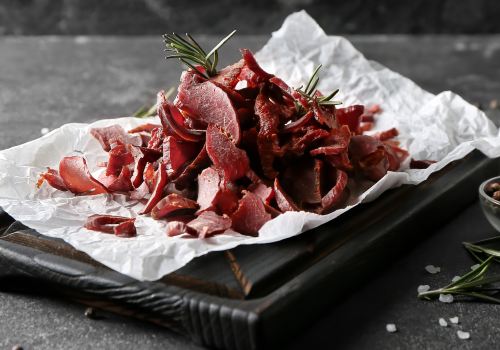 Thin curls of dried meat on a paper-lined black tray