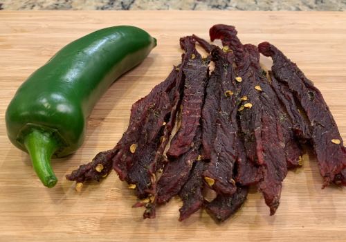 Finished jerky strips beside a whole green jalapeno
