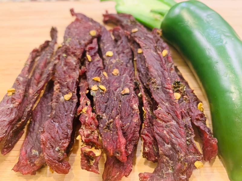 Jerky strips with pepper flakes beside a green jalapeno