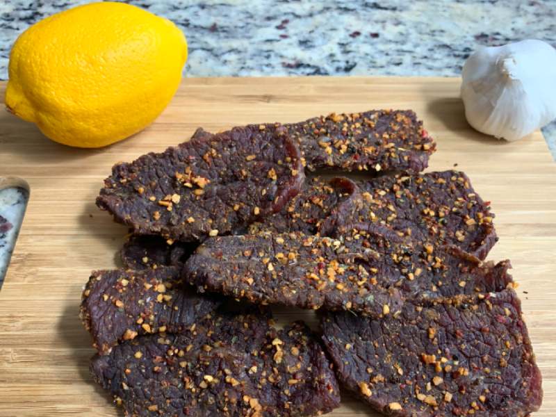 Beef jerky pieces coated with coarse spices beside lemon and garlic