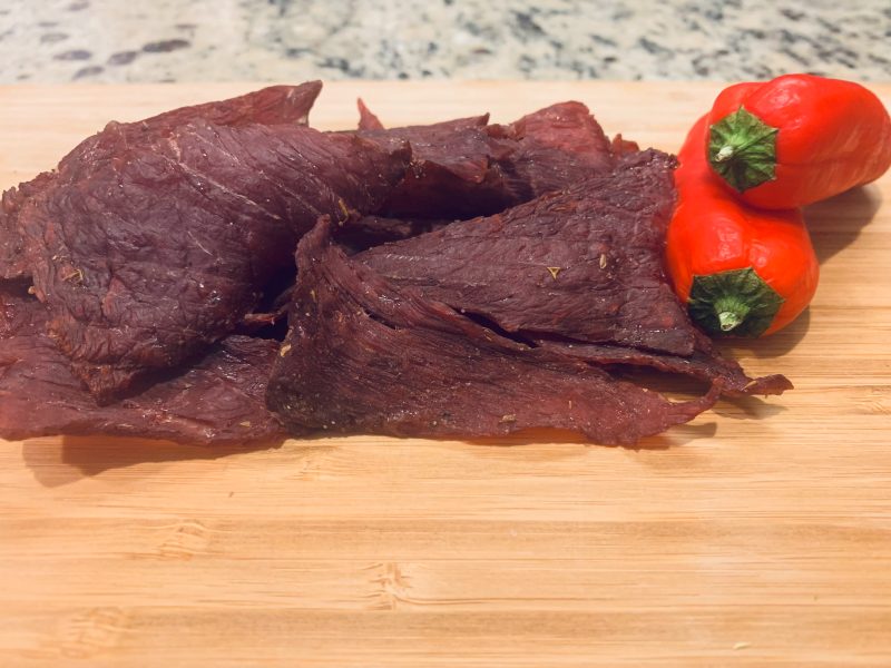 Wide homemade jerky pieces beside red peppers