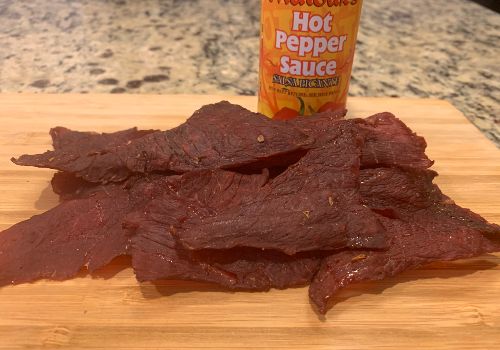 Wide strips of beef jerky beside a bottle of hot pepper sauce