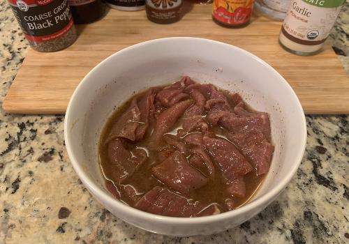 Wide beef pieces soaking in marinade in a white bowl