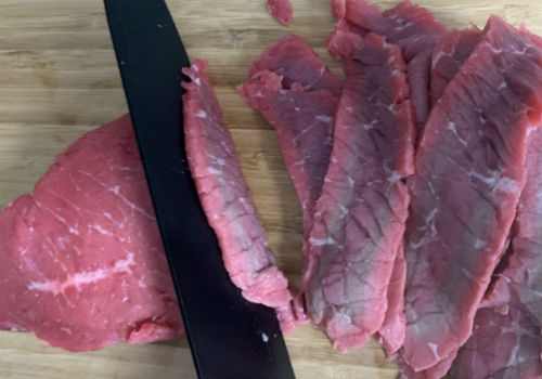 Knife slicing beef into narrow strips on a board