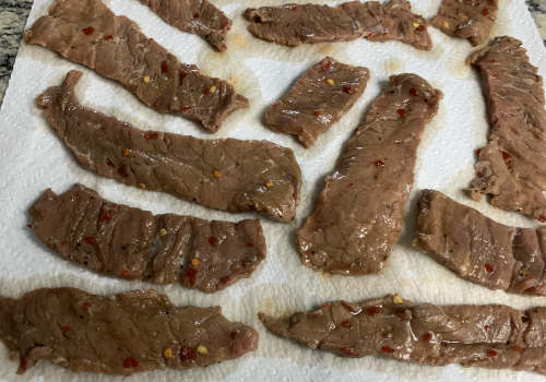 Marinated beef strips draining on paper towels