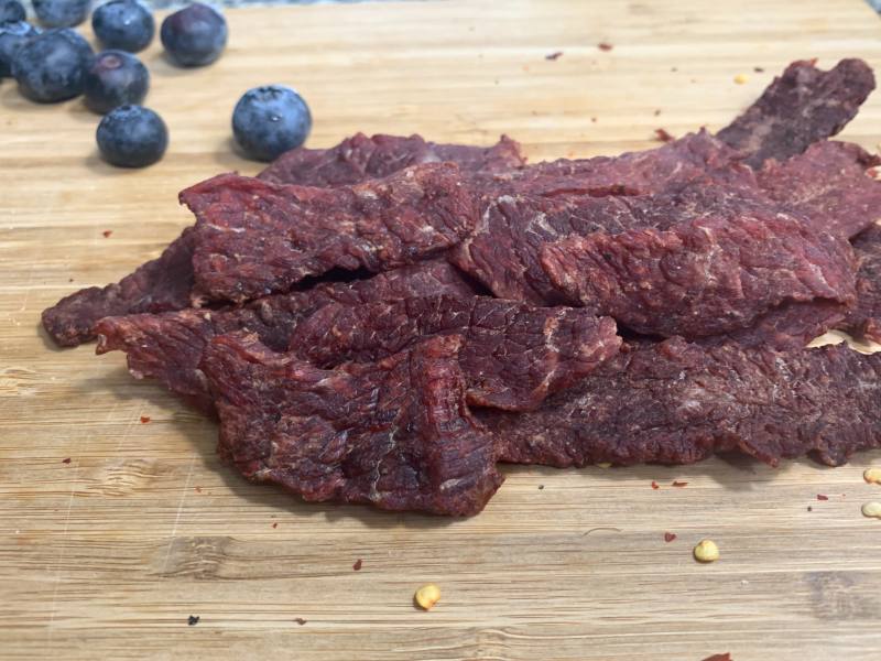 Beef jerky on a wooden board beside blueberries