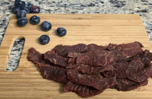 Sweet beef jerky piled on a board beside blueberries