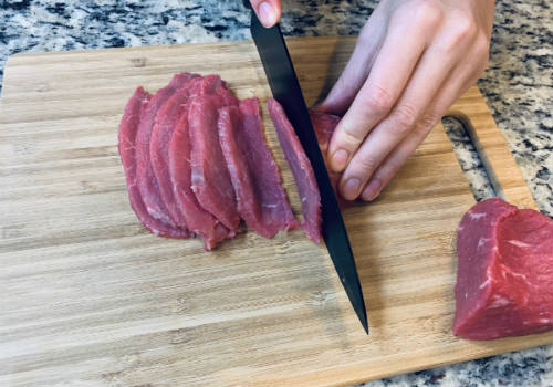 Knife slicing eye of round into thin pieces