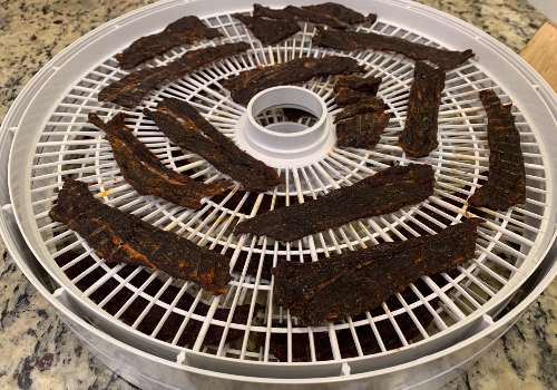 Darkened Sriracha beef jerky on a dehydrator tray