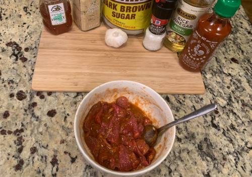 Beef strips in a bowl of red marinade beside Sriracha and seasonings