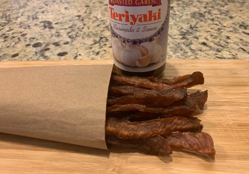 Pork jerky in an open paper bag beside teriyaki sauce